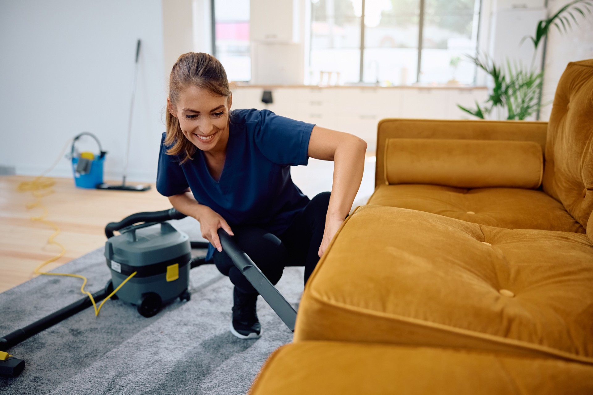 Happy housemaid using vacuum cleaner while cleaning sofa. Happy housemaid using vacuum cleaner while cleaning sofa.